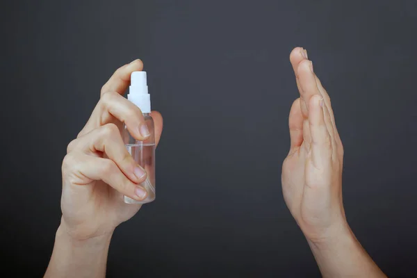 antiseptic bottle in hand, apply spray on hands on a dark background close-up, disinfection. concept hygiene