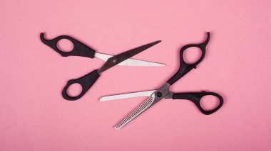 Pembe arka planda saç kesimi için iki çift makas.