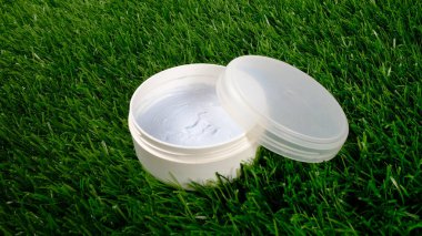 Güzelim, arka planda yeşil çimenler olan beyaz kavanozlu yakın plan. cilt bakımı kozmetikleri