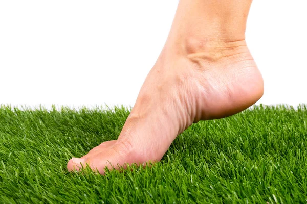 Bare foot touches the green artificial grass close-up on a white background — Stock Photo, Image