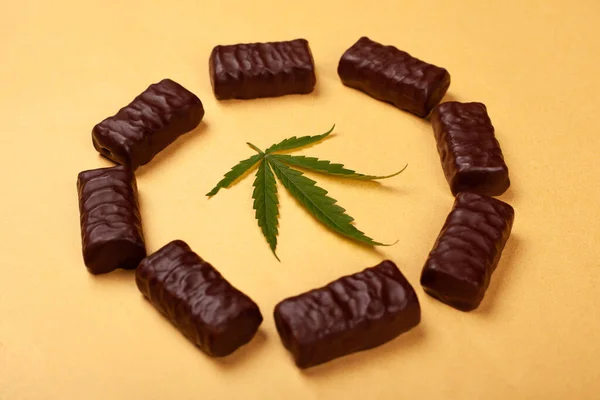 黄色の背景に緑の葉のマリファナ植物とチョコレートキャンディー。お菓子と大麻 — ストック写真