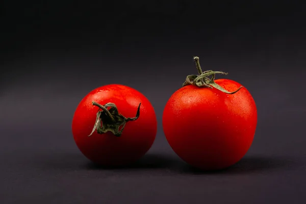 two red cherry tomatoes on a dark gray background