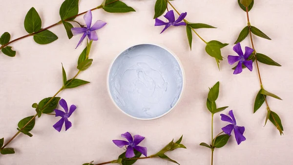Crema de belleza y flores violetas planas, vista superior sobre fondo blanco — Foto de Stock