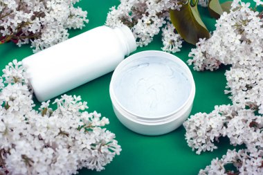 Cilt bakımı için beyaz şişeler ve yeşil arka planda beyaz leylak çiçekleri. Güzellik, kırışıklık önleme