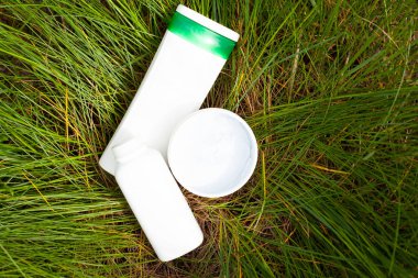 Yeşil çimlerin üzerinde, üzerinde vücut kozmetik ürünleri olan beyaz şişeler var. Güzellik, cilt bakımı, kırışıklık önleme, kaplıca