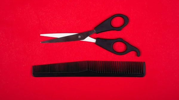 Black scissors and comb on a red background — Stock Photo, Image