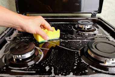 Kadın gaz sobasını çamaşır bezi ve köpükle temizliyor, yüzey temizliği, mutfağı ve mutfak aletlerini temizliyor.