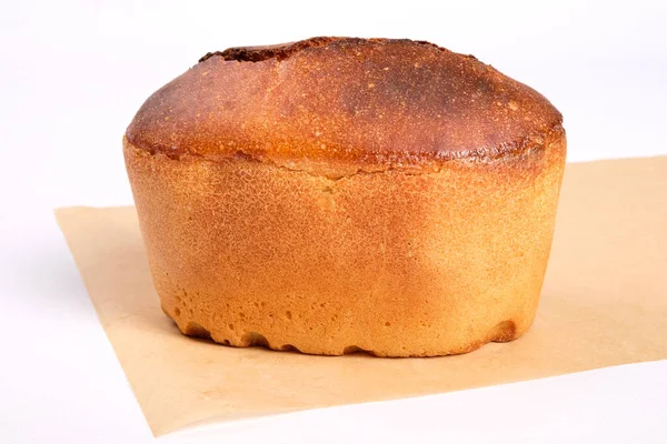 Pan de trigo recién horneado aislado sobre fondo blanco, productos de panadería, una hogaza de pan en una hoja de pergamino — Foto de Stock