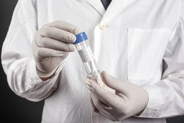 Dokter in witte vacht en wegwerphandschoenen met een container voor de levering van medische tests close-up, gezondheidszorgconcept — Stockfoto