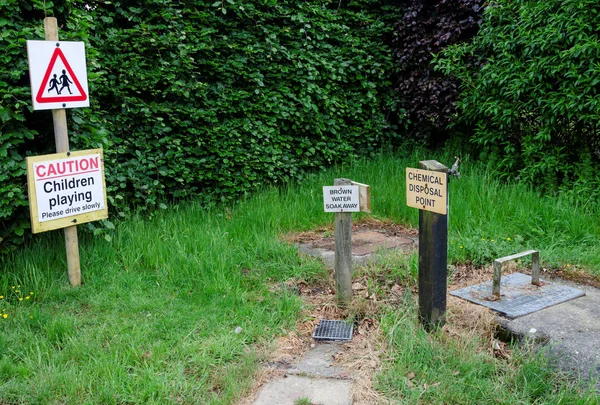 Chemical toilet and grey waste disposal point on a camp site with a warning sign for children nearby.