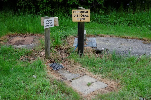 Chemical toilet and grey waste disposal point on a camp site with a warning sign for children nearby.