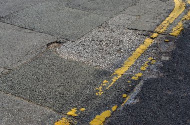 A road with double yellow lines. The road has been repaired by patching several times and is still in poor condition. clipart