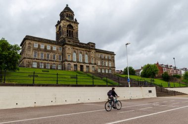 Wallasey, İngiltere: 23 Haziran 2020: Önünde The Memorial Gardens bulunan Wallasey Belediye Binası Hillsborough 'un 96 kurbanına adanmıştır. Bir bisikletçi geçiyor..