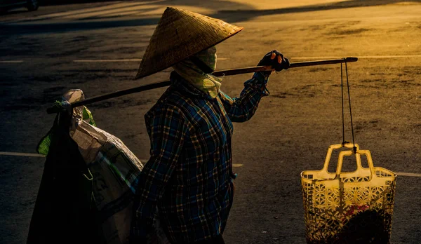 Vietnamilainen kartiomainen hattu kuljettaa ikeen olkapäällään pitkin katua . — kuvapankkivalokuva