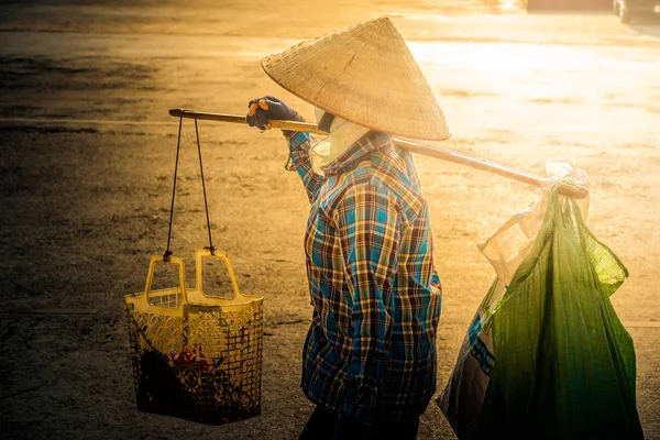 Vietnami kúpos kalapban egy igát hordozza a vállán az utcán. — Stock Fotó