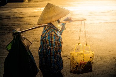 Cadde boyunca omzuna bir boyunduruk Vietnamca koni şapka ile taşır.