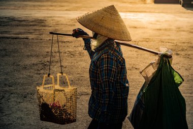 Cadde boyunca omzuna bir boyunduruk Vietnamca koni şapka ile taşır.