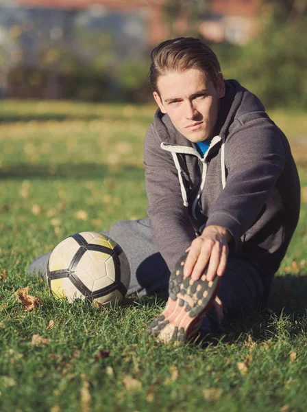 Soccer Player Stretching with Football in the Park on a Sunny Autumn Day