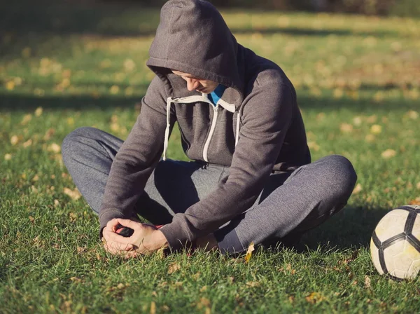 Soccer Player Stretching with Football in the Park on a Sunny Autumn Day