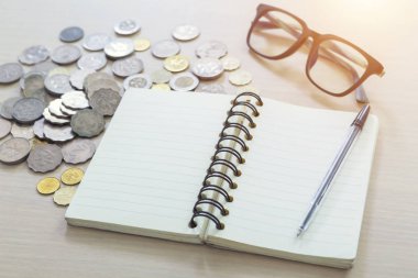 Boş not defteri, kalem, gözlük ve hafif bir arka plan üzerinde paralar.