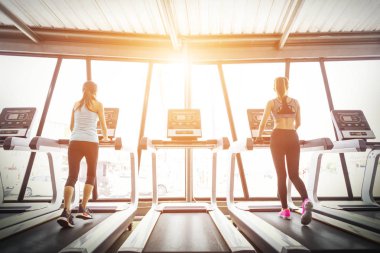 Güneş doğarken fitness salonunda treadmill çalışan spor kızlar.