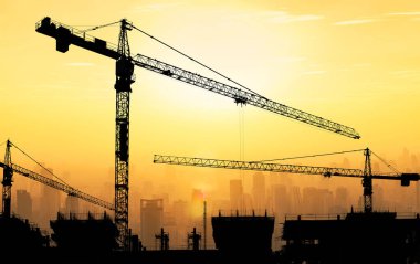 Büyük vinçler ve bina inşaatı ile cityscape arka planda güzel gölgeli günbatımı gökyüzü karşı.