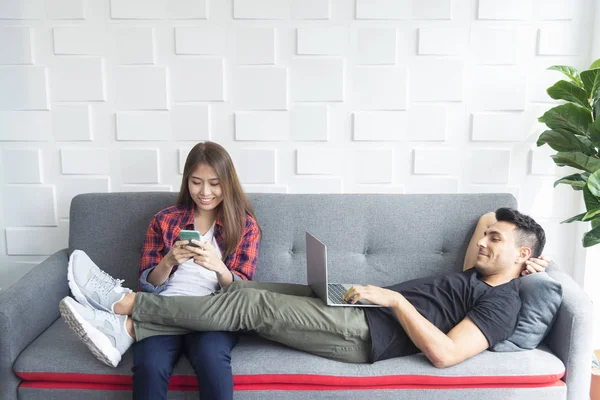 Couple relaxing on sofa at home. Using mobile and laptop to play, work and connect to another people in social media. Modern technology for life.
