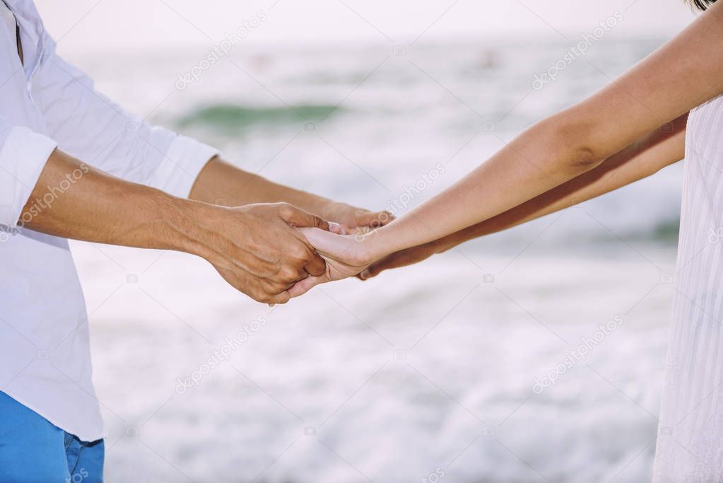 Closeup of couple holding hands togethers while walking on the b