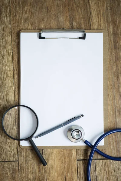 Magnifier with stethoscope on blank notebook on table. Medical b — Stock Photo, Image