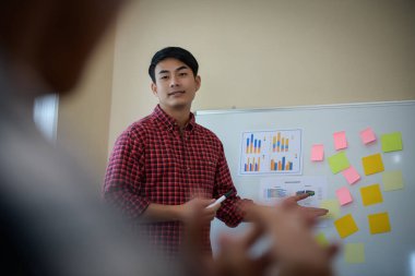 Handsome young man standing near whiteboard and pointing on the chart presentation perfect planning business with people group clapping.