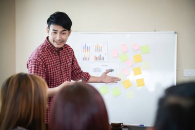 Handsome young man standing near whiteboard and pointing on the chart presentation perfect planning business with people group clapping.
