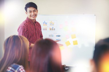 Handsome young man standing near whiteboard and pointing on the chart presentation perfect planning business with people group clapping.