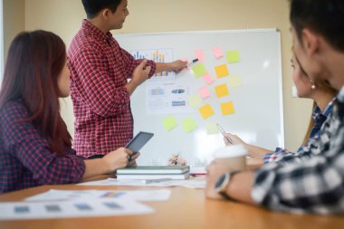Handsome young man standing near whiteboard and pointing on the chart presentation perfect planning business with people group clapping.