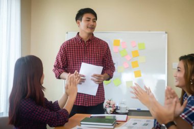 Handsome young man standing near whiteboard and pointing on the chart presentation perfect planning business with people group clapping.