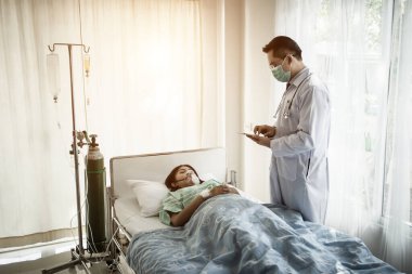 Hastanedeki hastaya bakarken doktor panoya yazı yazıyor..