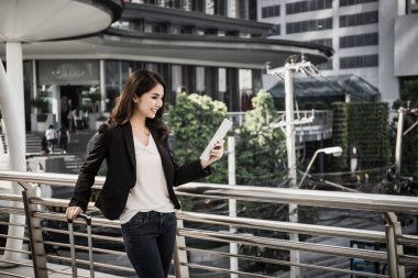 Güzel genç iş kadını toplu taşıma istasyonunun dışında yürüyor. Havaalanına giderken bavullu bir iş kadını gezgini..