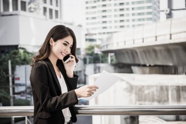 İşe giderken telefonla arayan ve belge okuyan meşgul bir kadın resmi