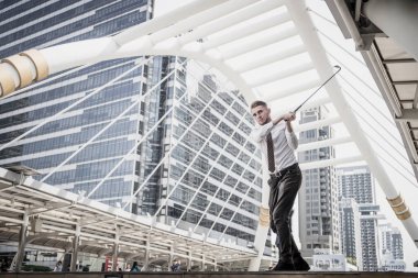 Arka planda şehir manzarasıyla golf oynayan iş adamının portresi. İş eğlencesi konsepti.