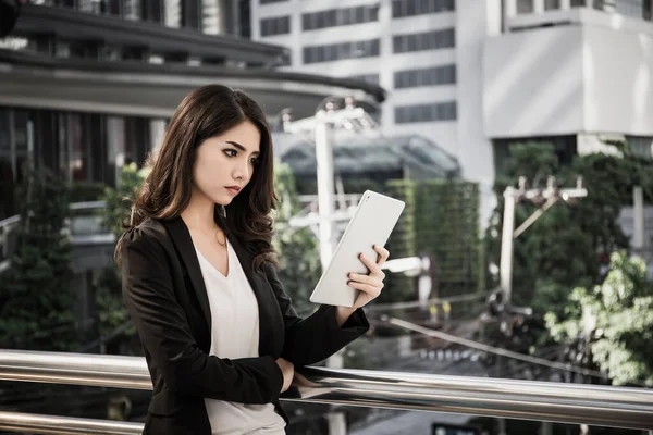 Attractive business woman using a digital tablet while standing in front of office building.