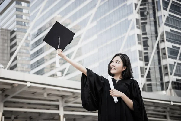 Portrait of young female graduates in square academic cap smiling happy holding diploma against building.