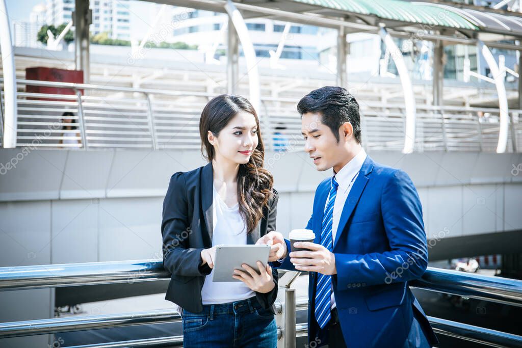 Business colleagues take a look at the work in the tablet while walking to the office together.