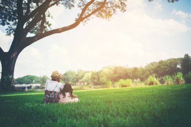 Genç anne ve kızı parkta yeşil çimlerde otururken rahatlıyorlar.