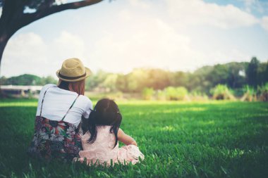 Genç anne ve kızı parkta yeşil çimlerde otururken rahatlıyorlar.