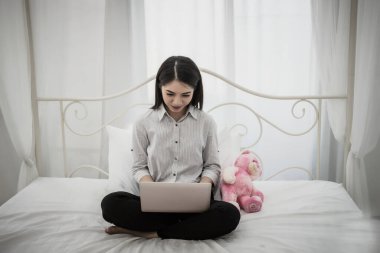 Evde yatakta oturmuş bir dizüstü bilgisayar üzerinde çalışan mutlu güzel kadın.