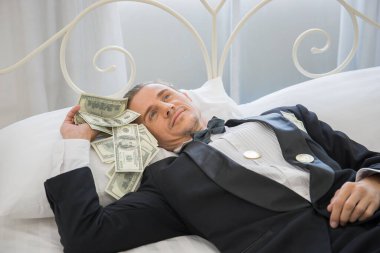 Dolar banknotlarıyla yatakta yatan zengin bir adam. Başarı iş konsepti.