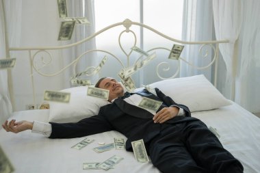 Dolar banknotlarıyla yatakta yatan zengin bir adam. Başarı iş konsepti.