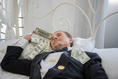 Dolar banknotlarıyla yatakta yatan zengin bir adam. Başarı iş konsepti.