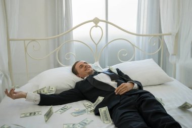 Dolar banknotlarıyla yatakta yatan zengin bir adam. Başarı iş konsepti.