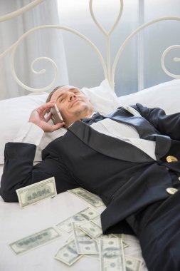 Dolar banknotlarıyla yatakta yatan zengin bir adam. Başarı iş konsepti.
