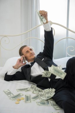 Dolar banknotlarıyla yatakta yatan zengin bir adam. Başarı iş konsepti.